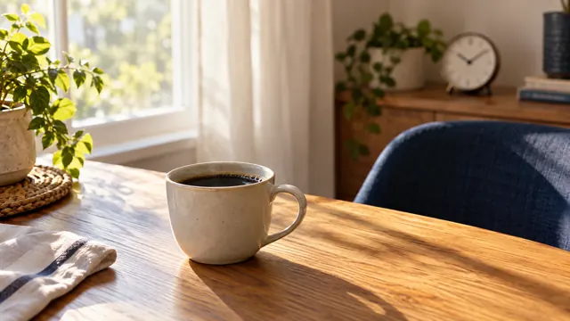 A cup of black coffee on a wooden table beside a sunny window